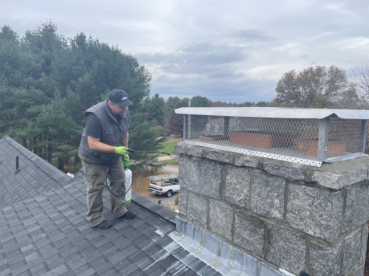 Technician spraying a chimney cap and crown on a stone chimney